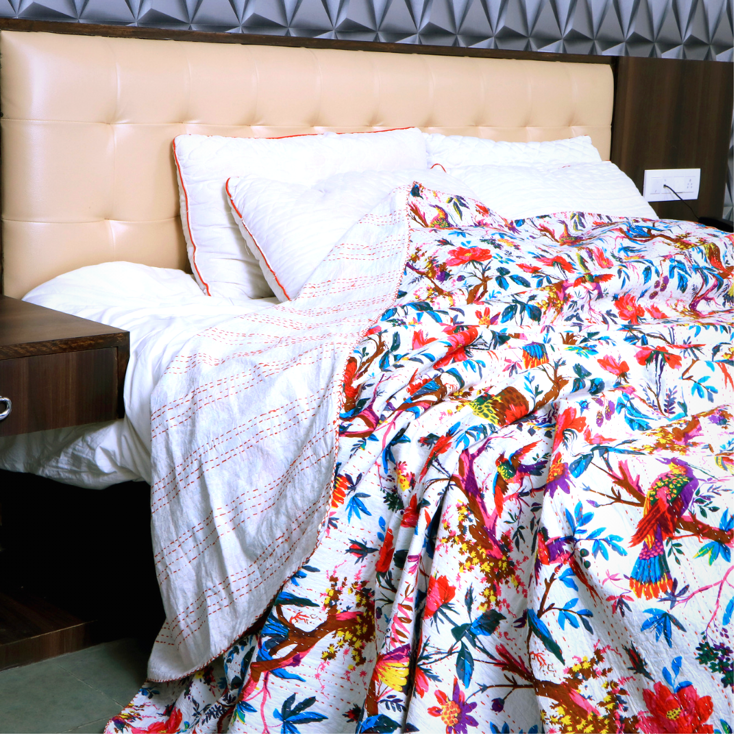 Colorful Bird of Paradise Kantha Blanket quilt with hand-stitched embroidery on a bed with pillows and beige headboard