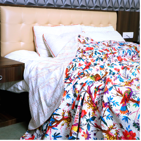 Colorful Bird of Paradise Kantha Blanket quilt with hand-stitched embroidery on a bed with pillows and beige headboard