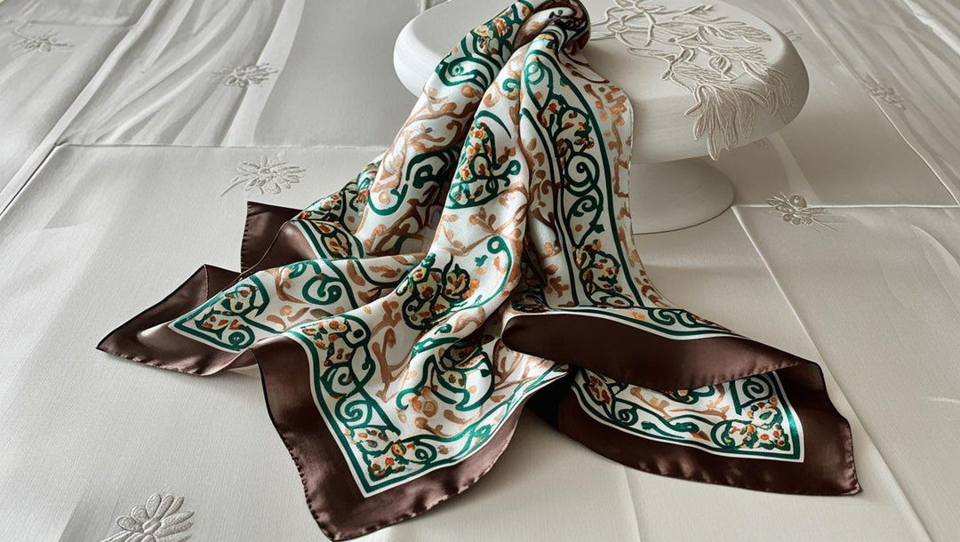 Hand-hemmed lightweight silk scarf with intricate green and brown floral patterns and a dark brown border on white background