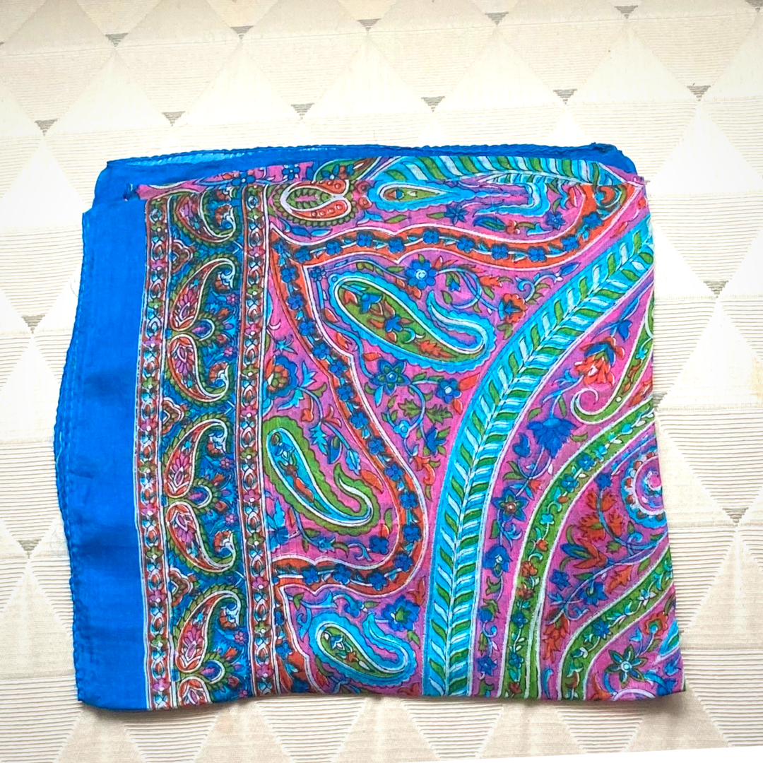 Brightly colored hand-hemmed silk scarf with intricate paisley design in blue, pink, and green tones, lightweight and luxurious accessory