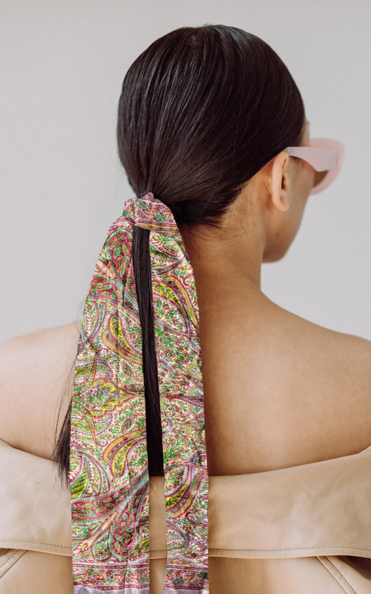 Luxurious hand-hemmed silk scarf in vibrant colors, styled as a hair accessory.