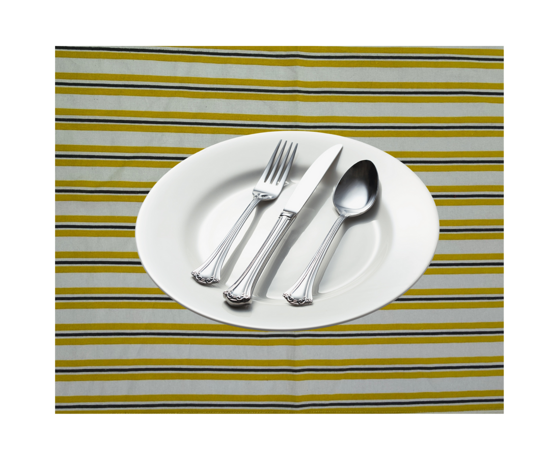 White plate with fork, knife, and spoon on yellow and gray striped cotton table linen.