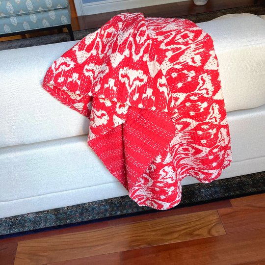 Red and white ikat design Kantha blanket draped over white sofa, lightweight hand-stitched cotton quilt